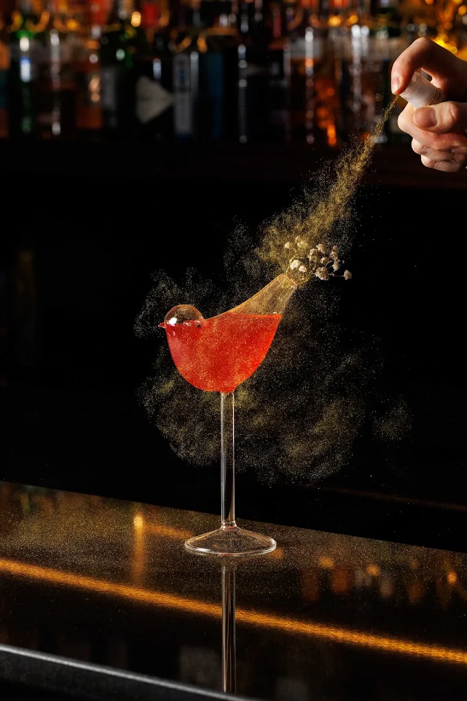 Cocktail garnish being dusted over a red cocktail